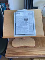 Front view of the KayJae wooden portable desk showing the adjustable tilted work surface with an informational sheet on top.