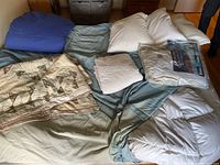 Wide view of entire bedding lot including quilts, duvets, pillow, mattress protector on bed