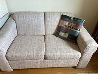 Full view of beige fabric single sofa bed with textured upholstery and one decorative pillow on the right side.