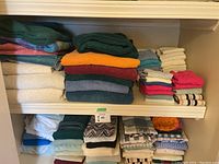 Wide view showing multiple stacks of assorted towels on two shelves, including bath towels, hand towels, kitchen towels, and facecloths in various colors and fabrics.