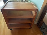 Front view of the wood wheeled cart showing three shelves with natural wood grain and caster wheels.