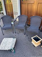 Three gray wicker patio chairs without cushions, cushions and planters nearby