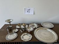 Wide view of assorted silverware laid out on table showing variety of cups, platters, trays, bowls, napkin rings.