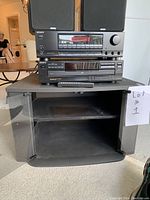 Full lot showing Sony stereo system on the TV stand with open shelf and glass doors, providing overall view of setup and items condition.