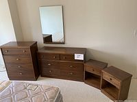 Wide view of the high boy dresser, low dresser, nightstands, and mirror arranged against a wall near a mattress.