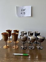 Set of 4 copper goblets and 6 silver plated goblets displayed on wooden surface with a pen for scale.