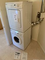 Full view of stacked washer and dryer with operating manuals on floor