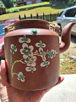 Front view showing handpainted plum blossom decoration on reddish brown Zisha clay teapot with bamboo handle.