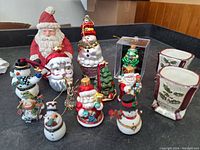 Photo shows 10 Christmas ornaments including various Santas, snowmen, elf, and boxed glass-blown frog, arranged on black surface.