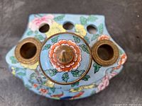 Top view of the porcelain enameled ink well showing floral patterns and three openings with bronze rims, as well as a lidded central compartment with a bronze finial.