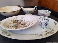 Assorted antique porcelain serving pieces arranged on a table including bowls, a sauce boat, and a small pitcher, all with floral patterns.