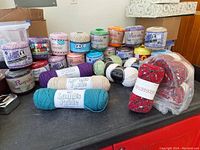 Overview of lot showing arranged colorful spools of crochet thread and yarn skeins on a black surface.