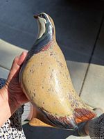 Side profile photo showing the detailed body and coloration of the ceramic quail sculpture held in hand.