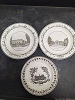 Three white porcelain plates with black transferware designs depicting historical Parisian buildings and street views, arranged on a dark surface.