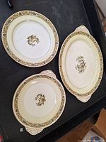 Three Johnson Brothers serving dishes laid flat: round plate, oval platter with handles, and shallow bowl. Pattern features floral and scroll in multiple colors with beige/gold border.