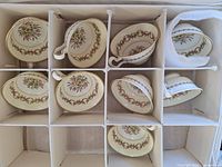 Nine Wedgwood teacups arranged in a cardboard box with dividers, showing the floral and gold pattern on each cup