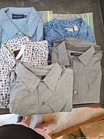 Lot of 5 men's button shirts, including long sleeve dress shirts and casual short sleeve denim shirts, folded and displayed on a table.