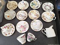 Overview of tea set comprising assorted Royal Albert teacups and saucers with different floral patterns and a milk pitcher.