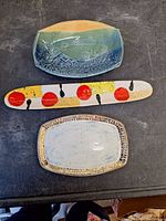 Top view of three pottery pieces on black surface: fish plate top, long olive dish middle, and rectangular bowl bottom.