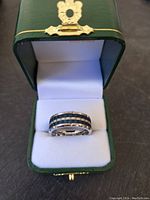 Front view of the men's tungsten carbide basketweave wedding band with navy blue accents, displayed inside a green Ken Walker Jewelers ring box lined with white padding.