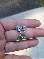 Hand holding two drop earrings with green tourmaline and white topaz gemstones in 925 silver.
