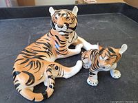 Front and side view of the larger and smaller porcelain tiger figurines on a black surface.