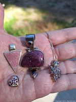 Four pendants and a sterling silver chain held in hand showing various semi-precious stones and silver settings