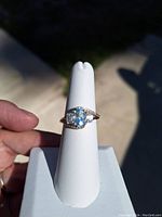 Close-up front view of sterling silver ring with pear-shaped light blue semi-precious stone and accent stones on band.