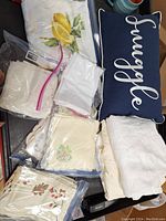Overall lot layout showing folded linens, some in ziplock bags, and decorative pillow with 'Snuggle' embroidery