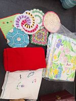 Overview of all items including crocheted pot holders, red napkins, embroidered linen, and floral sheets in packaging