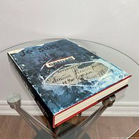Front and side view of the book on a glass table showing cover art and book thickness.