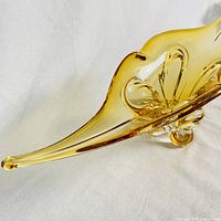 Close-up side view of amber art glass bowl showing elongated flowing form and smooth glass finish on white background.