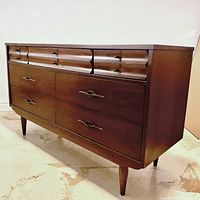 Angled view of full walnut dresser showing sculpted drawer fronts, brass pulls and tapered legs