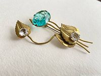 Photo of vintage Coro brooch angled to show blue and clear glass stones on gold-tone leaves