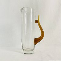 Full view of the clear tall glass pitcher with amber handle and small pouring spout.