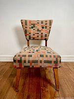 Front view of vintage MCM chair showing geometric upholstery and two green buttons on backrest.