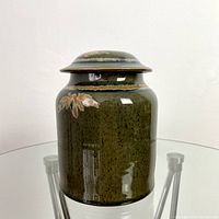 Side view of vintage signed lidded ceramic jar showing olive green glaze and floral decoration.