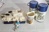 White G.I. Joe vehicle with 'United States' marking, G.I. Joe figure in front, and two G.I. Joe thermoses plus a ceramic mug on right side.