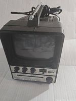 Front angled view of the Unisonic XL-900X portable TV showing the small black and white CRT screen, control knobs and switches, and raised antenna on top.