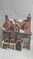 Front view of Dedlock Arms ceramic village building showing detailed windows, roof with snow patches, chimney stacks, entrance gate, and sign.