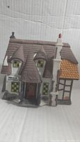 Front view of the Maylie Cottage porcelain village collectible showing detailed multi-roof structure and sign.