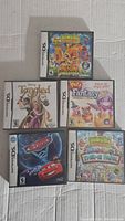 Photo of five Nintendo DS game cases showing titles Animal Jam, Tangled, My Little Pet Fantasy, Cars, and Toy Town Theme Park.