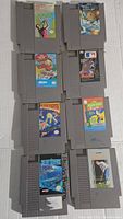 Front view of 8 different original Nintendo NES game cartridges laid out in two columns. Cartridge labels are visible showing game titles and artwork.