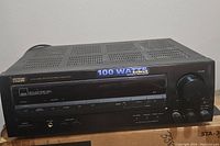 Front view of the black RCA STA-3850 stereo receiver showing control buttons, knobs, and headphone jack, with a blue label indicating 100 watts (note seller states 50 watts per channel).