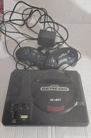 Sega Genesis console with two wired controllers and power adapter visible, showing overall lot contents.