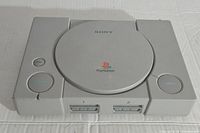 Top front view of original Sony PlayStation 1 console showing power, reset, and open buttons with the PlayStation logo on the round lid.