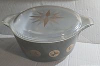 Overall photo showing opaque white casserole with dark band and gold zodiac symbols, and clear lid with starburst pattern.