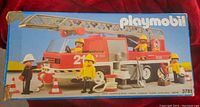 Front of the original Playmobil fire engine truck box showing the red truck, firefighter figures, and accessories arranged around the vehicle.