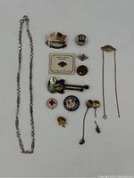 Full lot overview showing the necklace chain, mixed pins, and two gold items on right side.