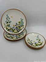 Set of eight plates displayed, four large dinner plates stacked with four smaller salad plates, showing floral pattern in blue, green, yellow and white with brown rims.